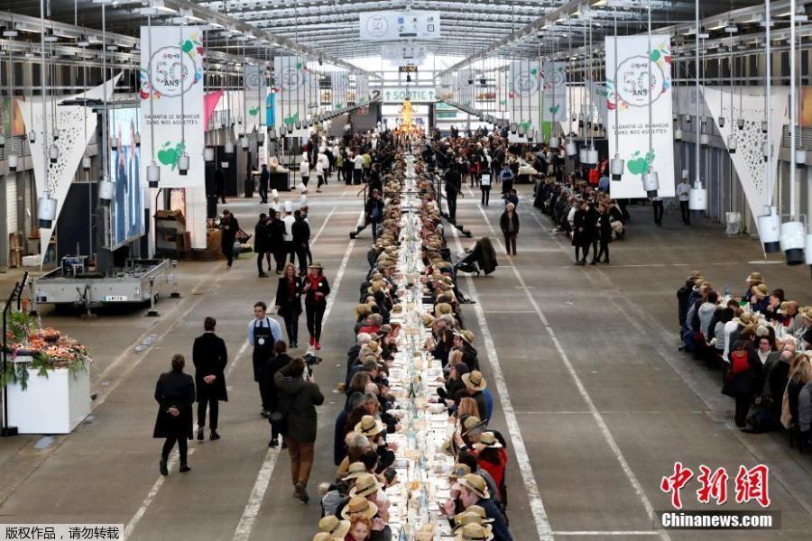 Participants attend a lunch served on a 401.22-meter-long table in the fruit and vegetable pavilion at the Rungis International Food Market during an event near Paris, France on March 17 celebrating the market’s 50th anniversary, which also aims to set a Guinness World Record.(Photo/Agencies)