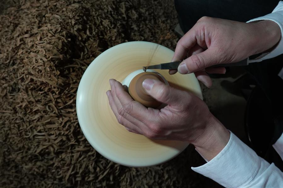 Chen Yufeng, inheritor of the workmanship of Jianzhan teaware, adjusts the shape of a piece of porcelain at his workshop in Jianyang District of Nanping City, south China\'s Fujian Province, March 28, 2019. Jianzhan teaware, a well-known Chinese porcelain originated in Jianyang, dates back to more than 1,000 years ago in Song dynasty (960-1279). It was the best teaware for scholars and literati to use during that time in tea competitions. Jianzhan teawares are known for their variability. Glazes can range in color from dark plum to yellow, green, and blue. During the heating and cooling processes, iron element in the clay can migrate within the glaze to form surface crystals in rich and glossy colors, as in the \