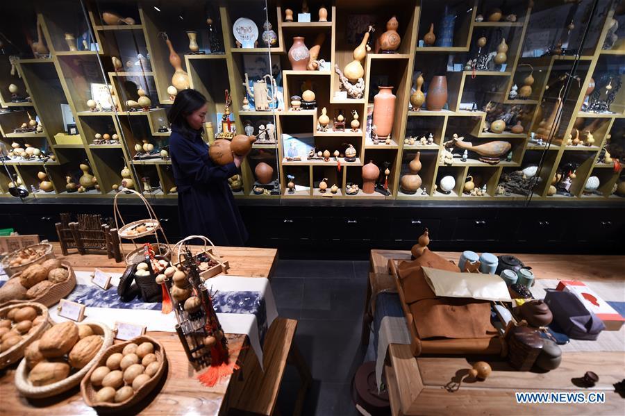 Ruan Xiyue, the fourth generation artist of Carved Gourd Ruan, arranges the handicrafts at a gourd carving studio in Lanzhou, northwest China\'s Gansu Province, April 1, 2019. A carved gourd, as the name suggests, is a gourd carved with landscapes, portraits, animals, calligraphy or poems, and then painted with ink. The process of gourd carving includes choosing gourd, painting, engraving and coloring. It was inscribed in the first group of provincial intangible cultural heritages of Gansu in 2006. (Xinhua/Fan Peishen)
