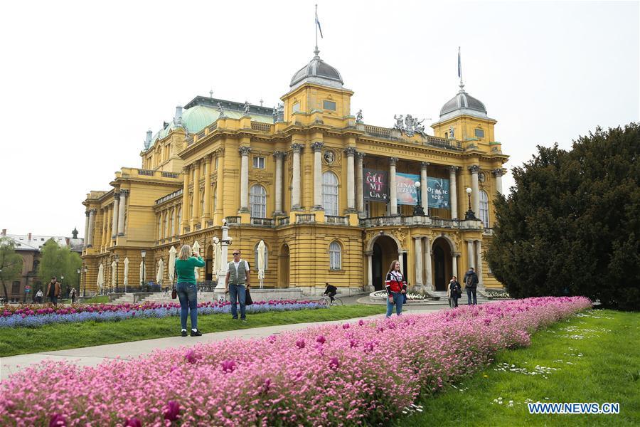 Photo taken on April 10, 2019 shows tourists taking photos with flowers outside the Croatian National Theatre in downtown Zagreb, capital of Croatia. (Xinhua/Zheng Huansong)