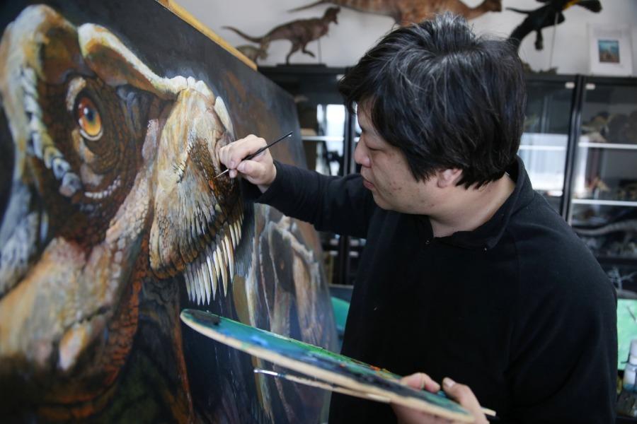 Zhao Chuang works on a dinosaur-themed painting in Shunyi district, Beijing. (Photo/China Daily)