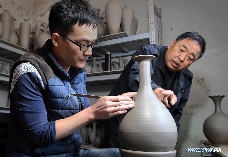 <?php echo strip_tags(addslashes(Wang Junzi guides his apprentice Li Jiabao at his studio in Qingliangsi Village, Baofeng County of central China's Henan Province, May 8, 2019. Ru porcelain, one of the five famous kinds of porcelains during the Song Dynasty (960-1279) in ancient China, is known for its azure color, light body, filmy grain and gentle textile. Wang Junzi, born in 1960, is a Ru porcelain firing craftsman in Qingliangsi Village of Baofeng County in central China's Henan, where the ancient official Ru porcelain kiln in Song Dynasty is located. In order to reproduce the beauty of 