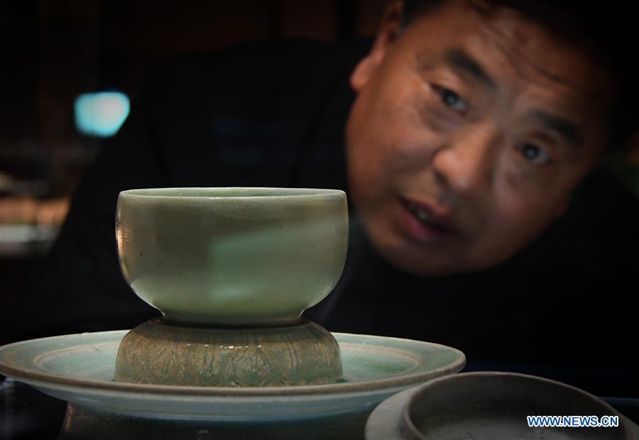 Wang Junzi exchanges with his apprentice Song Zhaobing on the traditional firing skills of Ru porcelain at the heritage site of Ru porcelain kiln in Qingliangsi Village, Baofeng County of central China\'s Henan Province, May 8, 2019. Ru porcelain, one of the five famous kinds of porcelains during the Song Dynasty (960-1279) in ancient China, is known for its azure color, light body, filmy grain and gentle textile. Wang Junzi, born in 1960, is a Ru porcelain firing craftsman in Qingliangsi Village of Baofeng County in central China\'s Henan, where the ancient official Ru porcelain kiln in Song Dynasty is located. In order to reproduce the beauty of \
