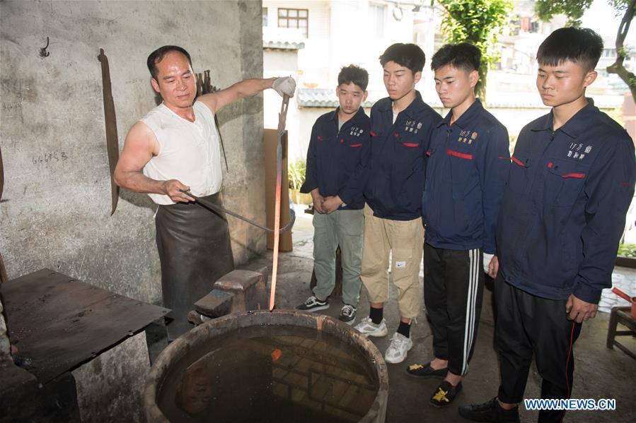 <?php echo strip_tags(addslashes(Zheng Guorong (L) teaches skills of sword making to his apprentices at Guyue Sword Studio in Longquan, east China's Zhejiang Province, May 21, 2019. For centuries, Longquan has been famed for its sword making industry. Zheng Guorong, 55, an intangible cultural heritage inheritor in Longquan Sword making, has been making sword for more than 30 years. Zheng regards sword as a symbol of spirit and devotes all to his career with awe. In his studio, the whole process of making a single sword takes two to three months, with steps including forming an idea, designing the sketch, preparing material and the final making and assembling. After setting up his studio, Zheng has trained more than 20 apprentices, who have all become sword smiths of great reputation. The old sword smith insists that Longquan sword, with a history of more than 2,500 years, deserves to be carried on in our time, both materially and spiritually. (Xinhua/Weng Xinyang))) ?>