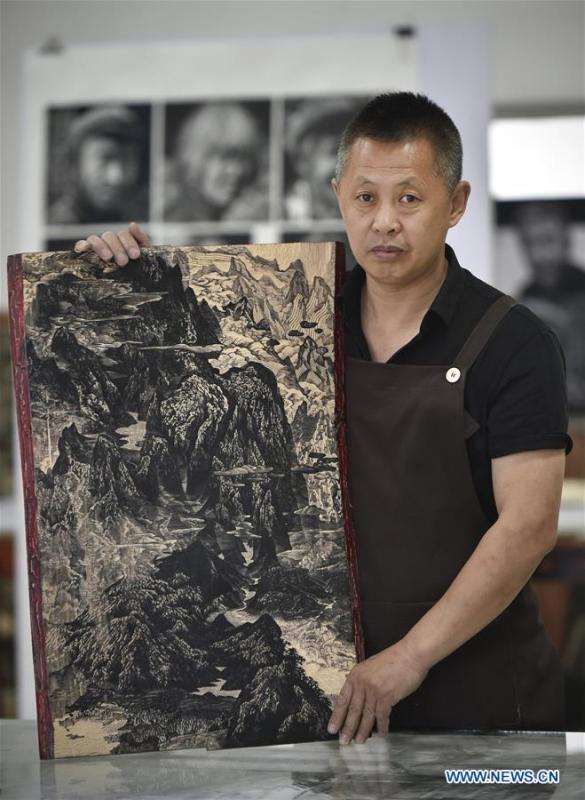 Chen Dongming demonstrates a recently-made wood-block painting at his studio in Huanren County of Benxi, northeast China\'s Liaoning Province, May 27, 2019. Chen Dongming, a 52-year-old wood-block painter from Wafang Village of Huanren County in Benxi, learned the techniques from his grandfather since young. As an inheritor of Huanren wood-block painting, a provincial intangible cultural heritage in Liaoning, Chen has been committed to making a proper integration of traditional Chinese landscape paintings and wood-block New Year paintings to promote the craft in an innovative way. (Xinhua/Yao Jianfeng)