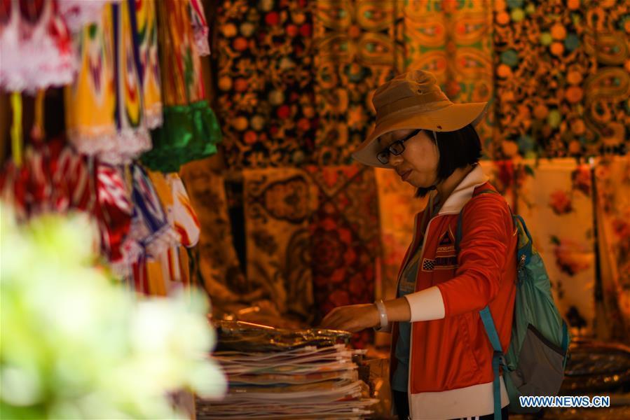 A tourist chooses handicrafts in the ancient city of Kashgar, northwest China\'s Xinjiang Uygur Autonomous Region, June 12, 2019. The ancient city of Kashgar has been well prepared for the peak tourism season through multiple measures including improving infrastructure and service quality as well as staging acrobatics performances to help tourists better experience the time-honored folk culture here. (Xinhua/Zhao Ge)