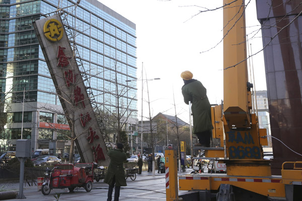 Workers remove a giant sign of a hotel in downtown Beijing last month that is deemed to have violated relevant regulations. (Photo by LIU MANQING/FOR CHINA DAILY)