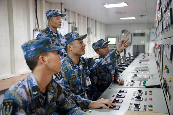 Senior Captain Lou Fuqiang (center), head of electric and mechanical facilities for Liaoning, the PLA navy's only aircraft carrier, checks the ship's equipment with crew members.  Han Feng / For China Daily