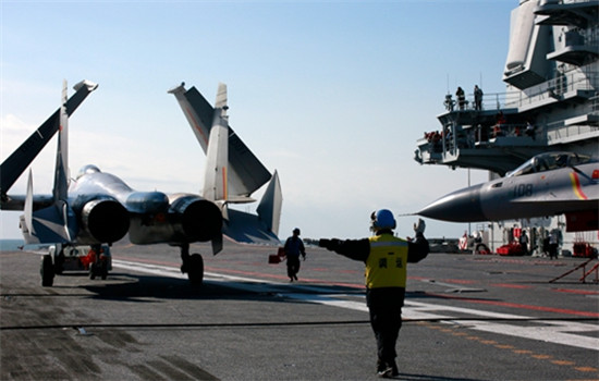 A member of the ground crew directs the pilot of a J-15 jet fighter on the flight deck of CNS Liaoning. (Zhang Kai / For China Daily)