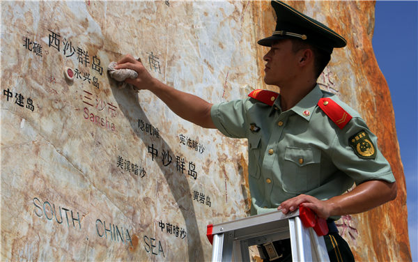 A guard cleans a stone map on Yongxing Island that indicates the locations of various districts of Sansha city, Hainan. (Photo by WEI TAOZE/CHINA DAILY)