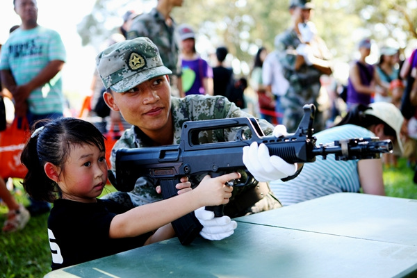 A soldier from the People's Liberation Army Hong Kong Garrison teaches a child to use a mock laser gun. ZHOU HANQING/CHINA DAILY