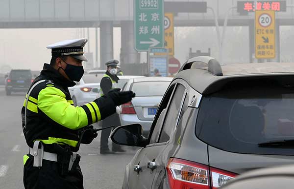 A traffic officer directs a driver at a toll station in Shijiazhuang, Hebei province, on Monday after the freeway linking Beijing and Hong Kong was partially closed due to heavy smog. ZHAI YUJIA/CHINANEWS SERVICE