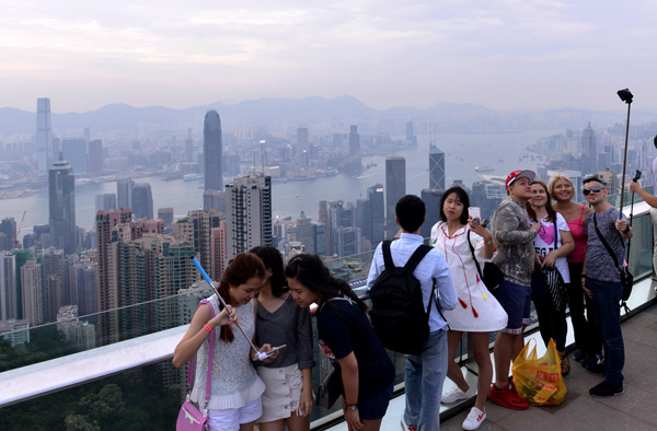 Visitors take selfies at Victoria Peak, using the harbor as a backdrop.(Photo by Yuan Shuiling/For China Daily)
