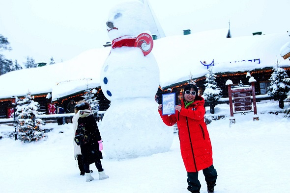 A Chinese tourist takes a photo with a snowman at a scenic spot in Finland.(Photo by Xu Kangping/for China Daily)