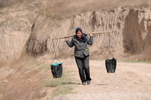 A woman carries two buckets of water fetched from three kilometers away in Tongwei county, Northwest China's Gansu province, April 5, 2013. Severe drought has lingered over most parts of the province since last winter, causing water shortages in many areas. [Photo by Liu Baocheng/Asianewsphoto]