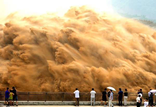 Tourists watch water gushing out from the Xiaolangdi Reservoir on the Yellow River during a sand-washing operation in Luoyang, Central China's Henan province, July 7, 2013. The on-going operation, conducted on Friday, works by discharging water at a volume of 2,600 cubic meters per second from the reservoir to clear up the sediment in the Yellow River, the country's second-longest waterway. Speeding currents would carry tons of sand into the sea. The Yellow River has been plagued by an increasing amount of mud and sand. Each year, the river bed rises as silt deposits build up, slowing the water flow in the lower reaches. [Miao Qiunao / Asianewsphoto]
