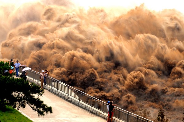 Visitors take photos of water gushing out of the Xiaolangdi Reservoir on the Yellow River in Central China's Henan province on Sunday in an annual operation to clear out the mud and sand accumulated at the dam. [Miao Qiunao / Asianewsphoto]