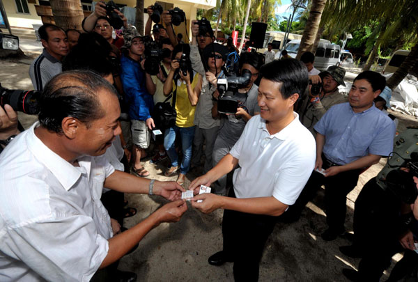 Feng Wenhai, center, vice-mayor of Sansha city, hands out residence permit cards to residents, July 17, 2013. [Photo/Xinhua]