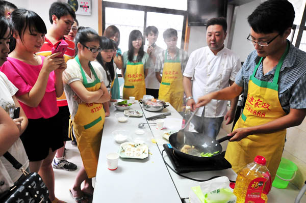 More than 30 college students, half of them male, learn how to cook while training to be domestic helpers in Fuzhou, Fujian province, on July 16, 2013. The training includes child care, pregnancy care and cooking skills. The students will hit the rising demand for domestic service summer internships after they get their certificates. [Photo by Zhang Bin/Asianewsphoto]