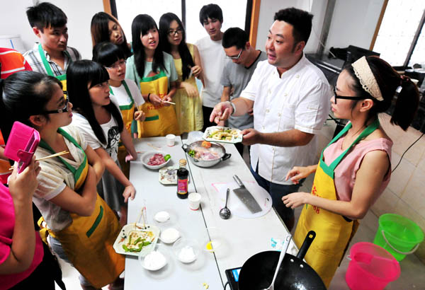 More than 30 college students, half of them male, learn how to cook while training to be domestic helpers in Fuzhou, Fujian province, on July 16, 2013. The training includes child care, pregnancy care and cooking skills. The students will hit the rising demand for domestic service summer internships after they get their certificates. [Photo by Zhang Bin/Asianewsphoto]