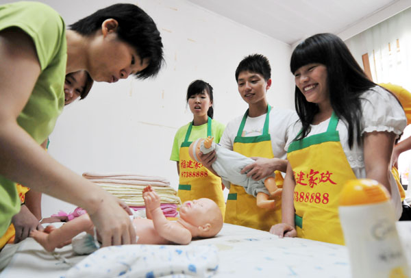 College students receive training in baby care to be a certificated domestic helper in Fuzhou, Fujian province, on July 16, 2013. [Photo by Zhang Bin/Asianewsphoto]