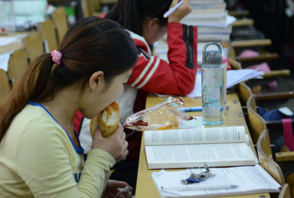 A college student nibbles a snack with her eyes still glued to her books in Taiyuan, Shanxi province, Oct 29, 2013. [Photo by Liu Jiang/Asianewsphoto]