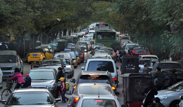 Pedestrians move through parked and running vehicles near South Third Ring Road in Beijing, Nov 14, 2013. The city has almost 5.4 million motor vehicles and only 2.76 million parking spaces. The capital will issue 150,000 license plates next year, down from 240,000 this year, to try to limit the number of cars and curb air pollution. [Photo/Xinhua]