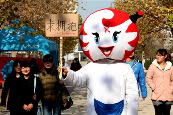 A college student in Bozhou, Anhui province, dressed in a costume, holds up a sign that reads, I would like to hug people infected with HIV, Nov 28, 2013. College students launched a campaign calling for the elimination of discrimination against people with AIDS. World AIDS Day is Dec 1. [Photo by Liu Liqin/Asianewsphoto]