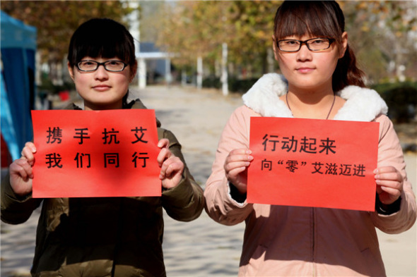 College students in Bozhou, Anhui province, hold up signs that read, Let's be united to combat HIV, Nov 28, 2013. [Photo by Liu Liqin/Asianewsphoto]