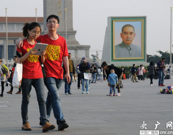 Tourists walk in front of a huge Sun Yat-sen portrait displayed on Tian'anmen Square ahead of the three-day May Day holiday in Beijing on April 27, 2014. [Photo: CNR]