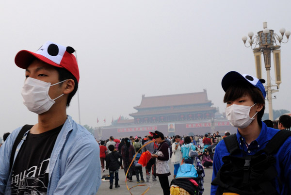 Tourists wear face masks to protect them from heavy smog as they visit Tiananmen Square in Beijing on Saturday. Wen Bao / For China Daily