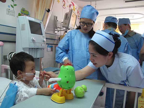 A nurse talks with a child of the Qiong ethnic group, who just had a surgical operation for congenital heart disease, at the Chengdu Military General Hospital.(Photo by Huang Zhiling/China Daily)
