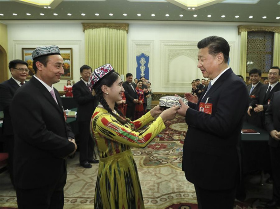 Chinese President Xi Jinping receives a traditional Uygur hat, a gift symbolizing the highest respect and best wishes from people of all ethnic groups in Xinjiang, when joining a panel discussion with deputies to the 12th National People's Congress (NPC) from Xinjiang Uygur Autonomous Region at the annual session of the NPC in Beijing, capital of China, March 10, 2017. (Xinhua/Lan Hongguang)