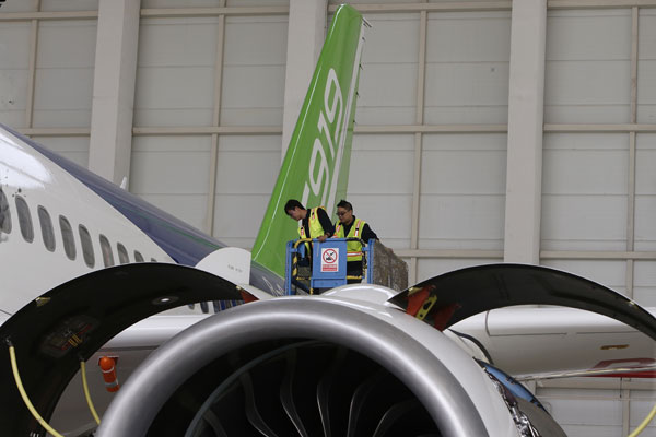 Two technicians inspect an engine on the C919, China's first domestically produced single-aisle passenger jet, after a taxiing test on Wednesday.(Photo by Yin Liqin/China Daily)