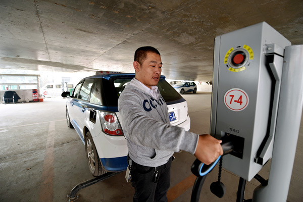 A taxi driver charges his electric vehicle at a charging post in Taiyuan, Shanxi province, on Oct 19. The city initiated a move last year to replace gasoline and hybrid taxis with purely electric ones. Currently, 97 percent of taxis in the city are purely electric. (Photo by Zhan Yan/Xinhua)