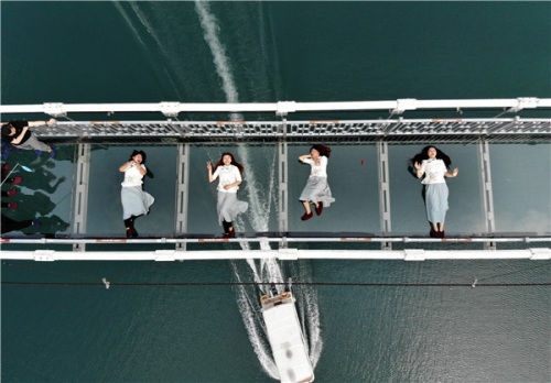 Four waitresses lie down for a photo on a glass bridge in Shiyanhu Ecological Tourism Park in Changsha, Hunan province, on Friday. Some grassroots workers, including street cleaners, chefs and security guards, are invited to the park to showcase their skills and pose for creative pictures, ahead of the May Day holiday. (YANG HUAFENG/CHINA NEWS SERVICE)